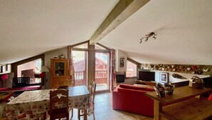 Una habitación acogedora en el ático con una mesa de comedor, sillas, un sofá rojo y un televisor.