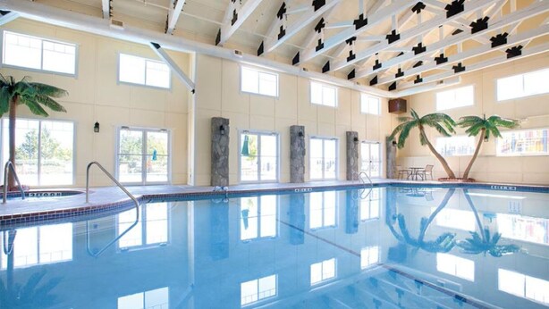 Une vaste piscine intérieure à l’eau d’un bleu cristallin, agrémentée de piliers en pierre et de palmiers.
