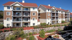 Un immeuble résidentiel à plusieurs étages, doté de balcons, d’un mur de soutènement en pierre et de jardins aménagés.