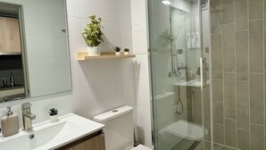 Un baño moderno con inodoro, lavamanos y ducha con mampara de vidrio.