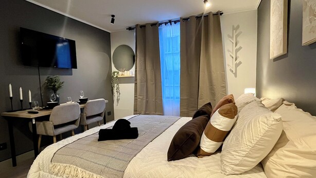 Un dormitorio moderno con una cama grande, un escritorio con silla, un televisor de pantalla plana y una ventana con cortinas.