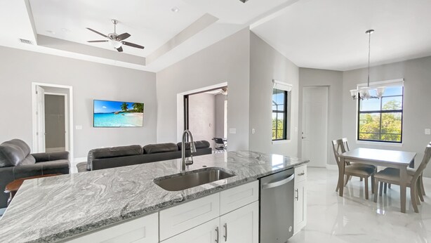A modern kitchen with a marble countertop, stainless steel sink, and white cabinetry. - Sweet Retreat, Sleeps 6, heated salt pool (Port Charlotte)