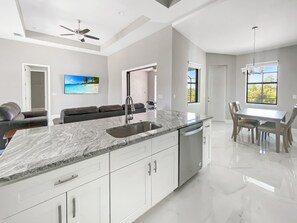 A modern kitchen with a marble countertop, stainless steel sink, and white cabinetry. - Sweet Retreat, Sleeps 6, heated salt pool (Port Charlotte)