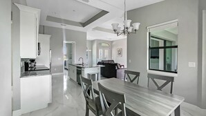 A modern kitchen with white cabinets, a dining area with a wooden table and chairs, and a large window with a view. - Sweet Retreat, Sleeps 6, heated salt pool (Port Charlotte)