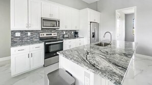A modern kitchen with white cabinets, stainless steel appliances, and a granite countertop. - Sweet Retreat, Sleeps 6, heated salt pool (Port Charlotte)