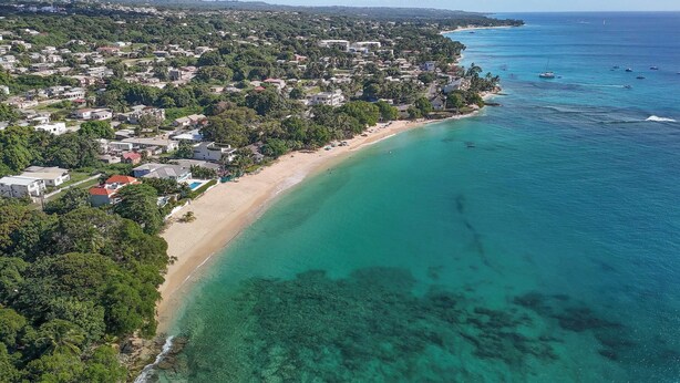Ein Luftbild einer Küstenstadt mit einem langen Sandstrand, klarem türkisblauem Wasser und üppiger Vegetation.