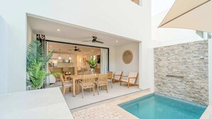 Ein moderner Poolbereich im Freien mit Essgruppe, Steinmauer und Deckenventilatoren.