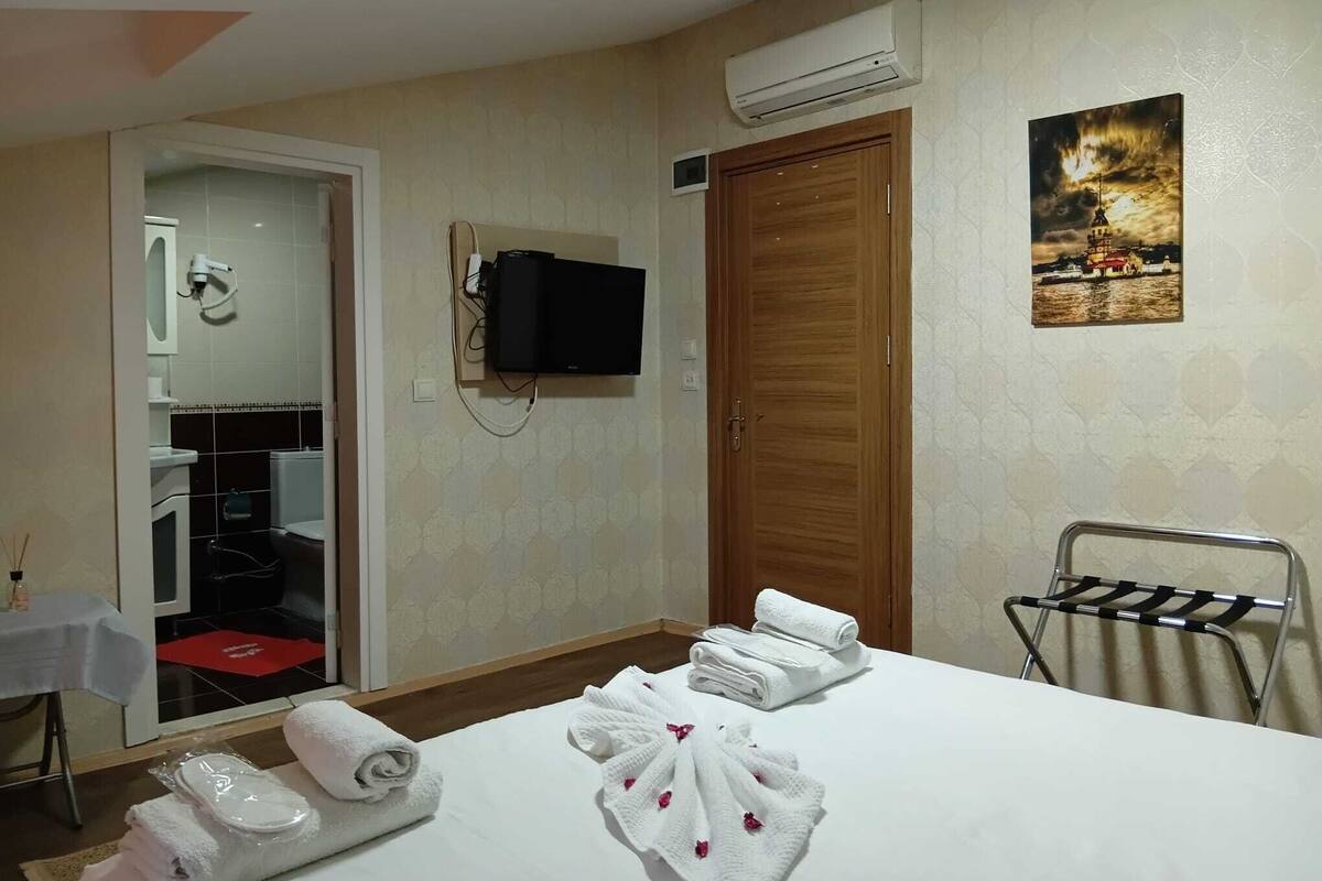 A hotel room with a bed, a TV mounted on the wall, a wooden door, and a painting of a cityscape.