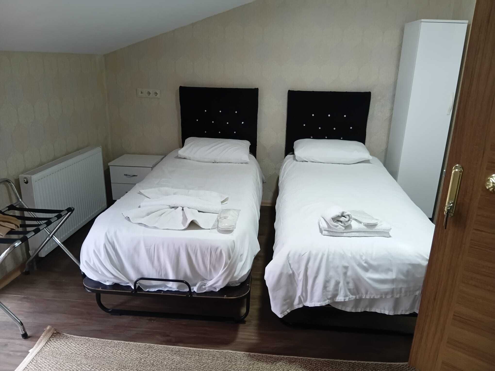 A room with two beds, each with white linens and pillows, a radiator, a small bedside table, and a wooden door.
