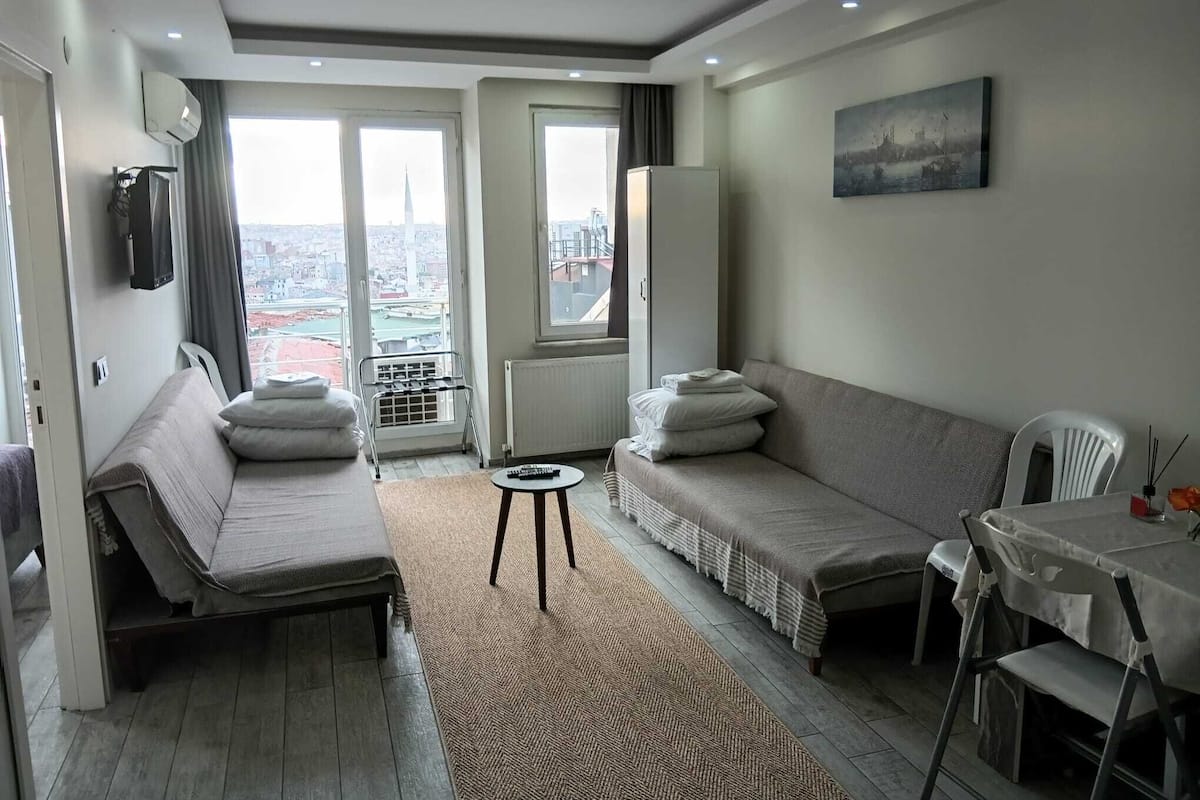 A modern hotel room with a sofa, a small table, and a view of the city through large windows.