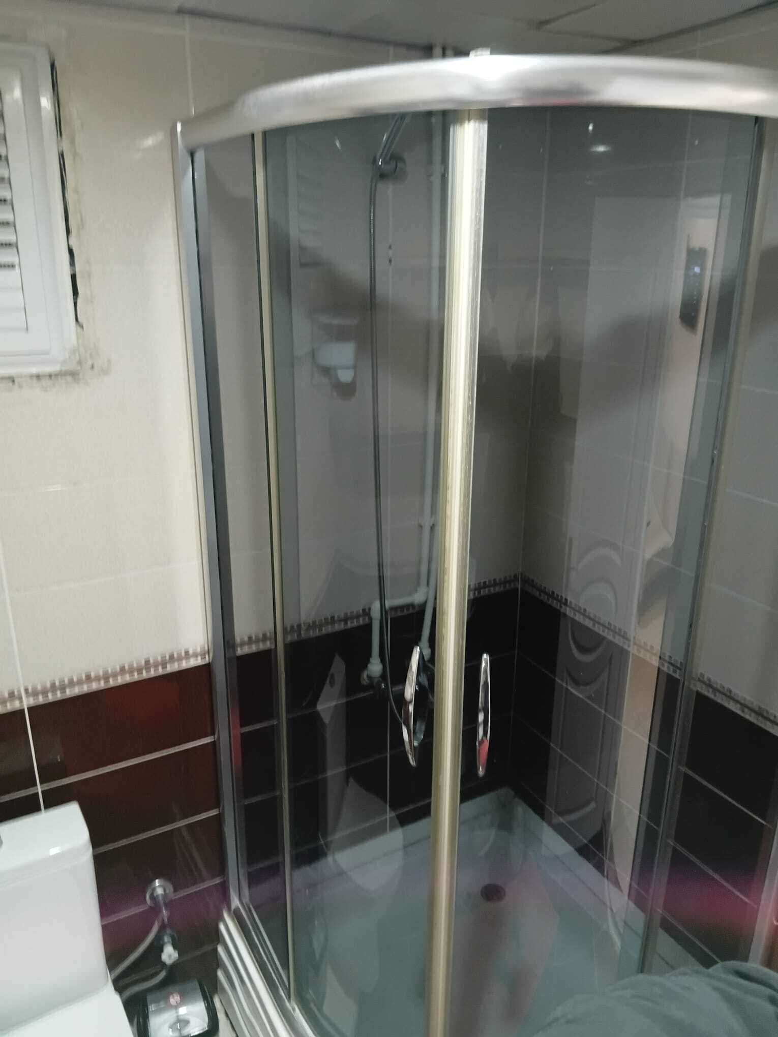 A glass-enclosed shower stall with a white ceiling and tiled walls.