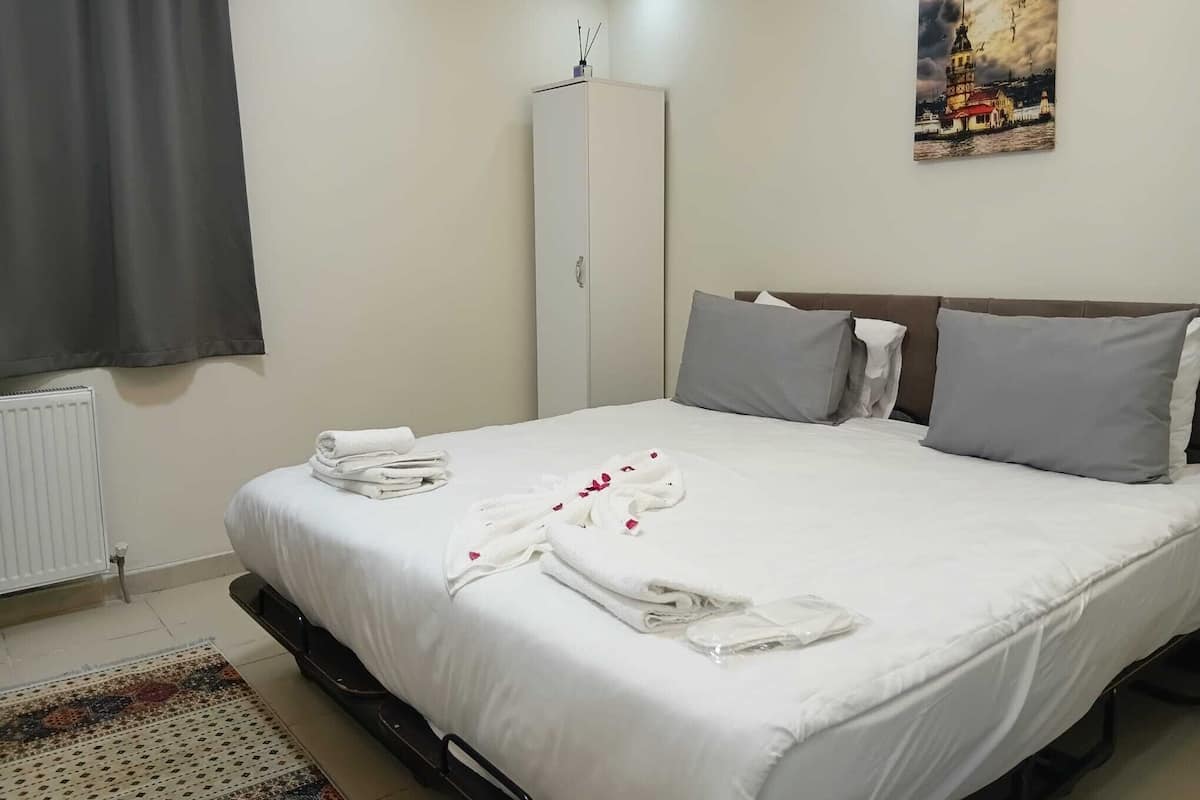 A hotel room with a bed, pillows, a radiator, a wardrobe, and a painting on the wall.