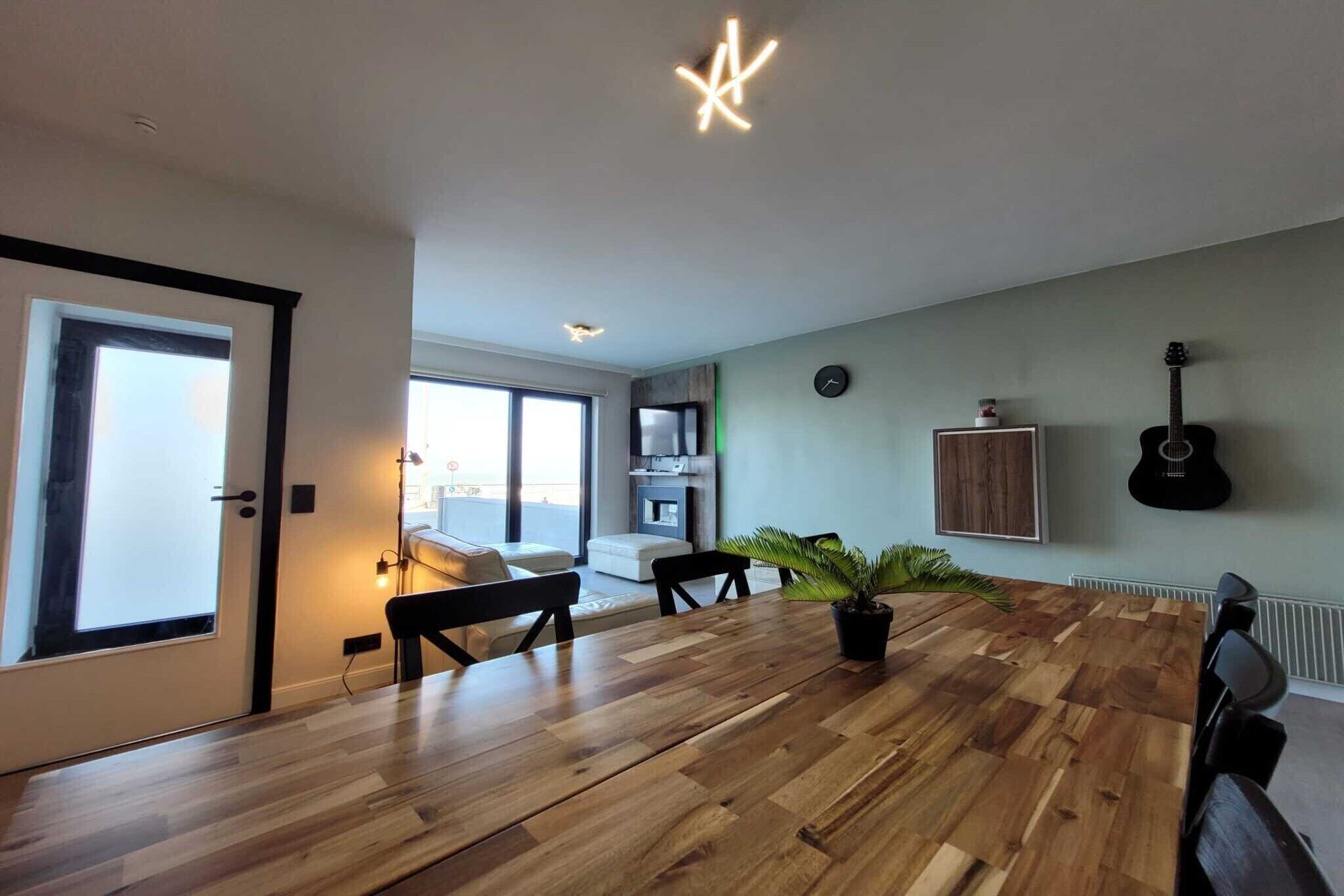 A modern living room with a wooden dining table, a potted plant, and a guitar on the wall.