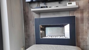 Un dormitorio moderno con una cama grande, televisor integrado y una repisa sobre la cama.