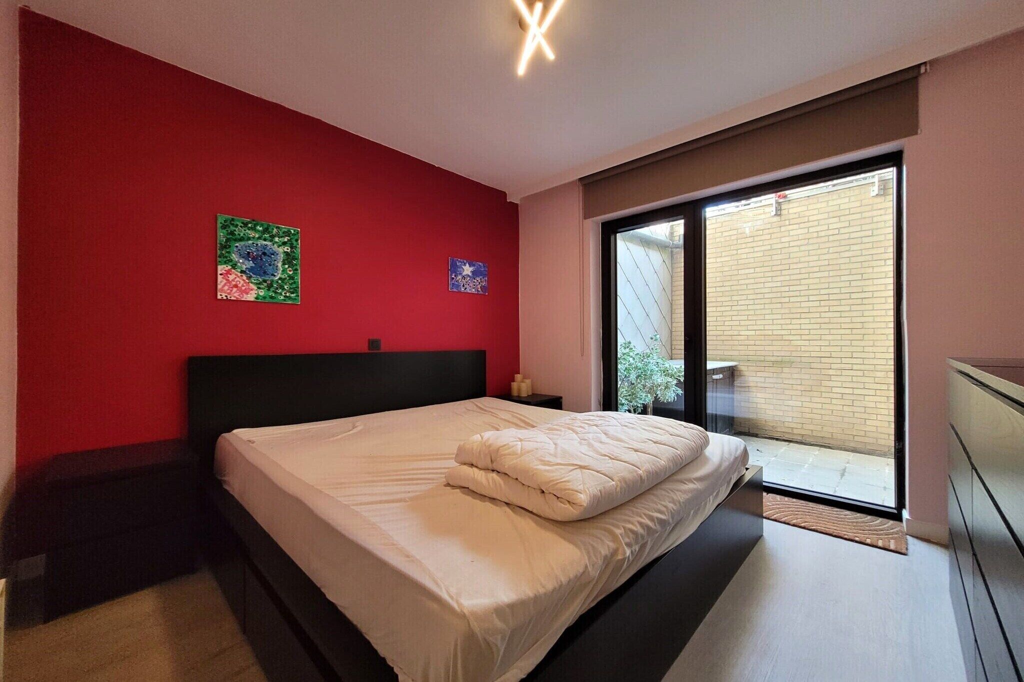 Un dormitorio con cama, pared roja y puerta corrediza de vidrio a un balcón.