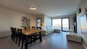 Una sala de estar moderna con una mesa de comedor de madera, sillas negras, un sofá blanco y un amplio ventanal con vistas.