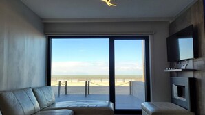 Una sala de estar moderna con un amplio ventanal corredera que da a un balcón con vistas a la playa.