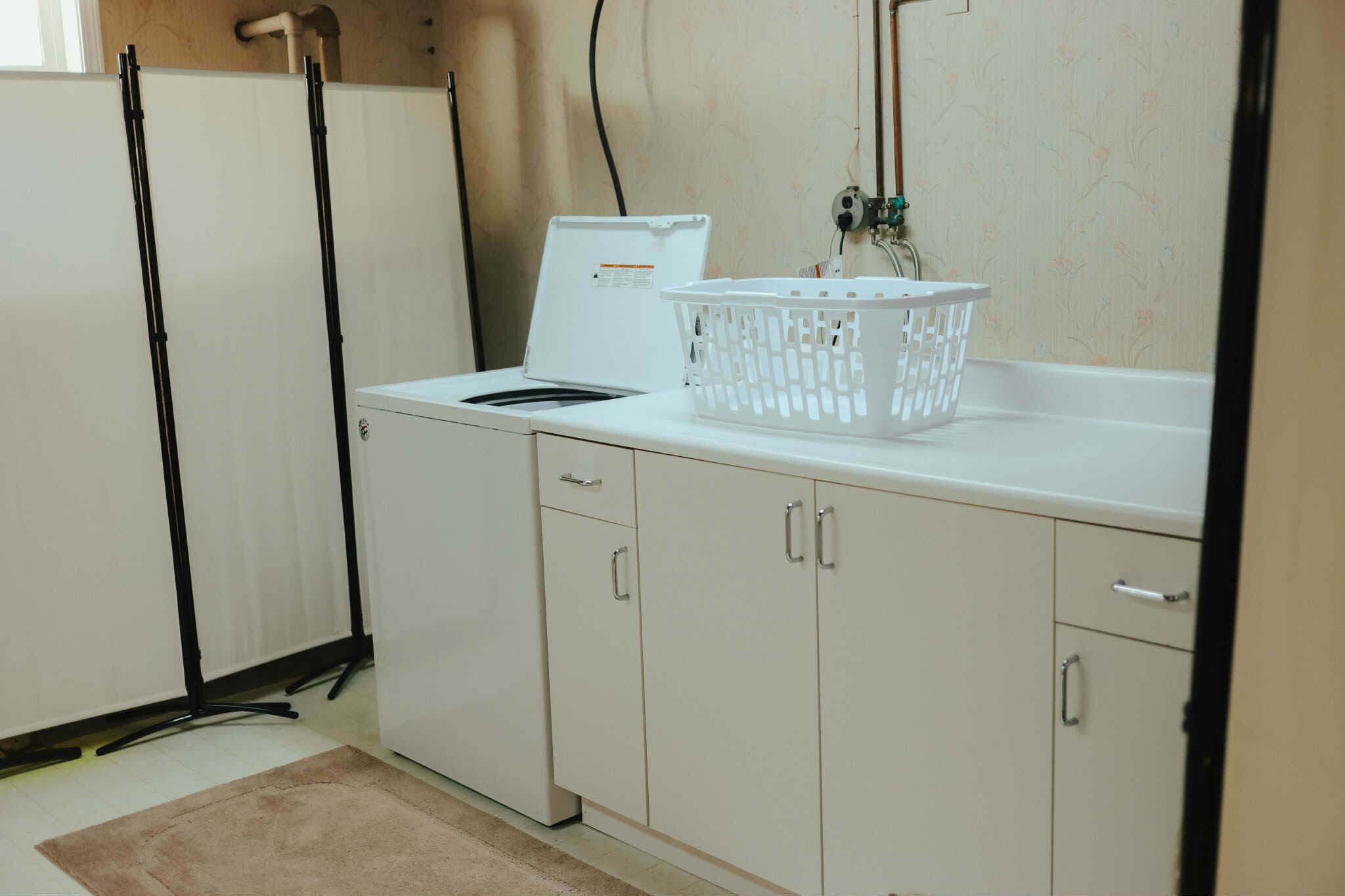 Une cuisine avec des meubles blancs, un plan de travail blanc, un panier à linge blanc et un appareil électroménager blanc.