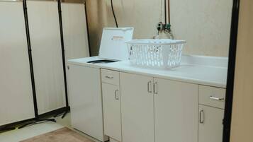 Une cuisine avec des meubles blancs, un plan de travail blanc, un panier à linge blanc et un appareil électroménager blanc.