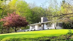 Ein Haus mit einem geneigten Dach, einer überdachten Veranda und einem gepflegten Rasen.