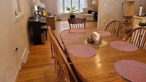 Ein Essbereich mit Holztisch, Stühlen und Untersetzern. Im Hintergrund befindet sich eine Couch und ein Fenster mit Vorhängen.