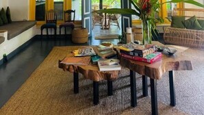 Un vaste espace de vie agrémenté d’un grand luminaire suspendu en fibres tressées, d’une table centrale avec des livres et d’un coin salon confortable.