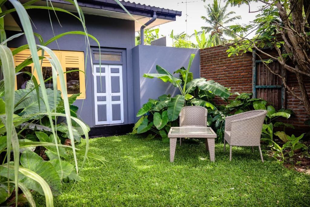 A house with a grey exterior, a white door, and a small patio area with two wicker chairs and a table.