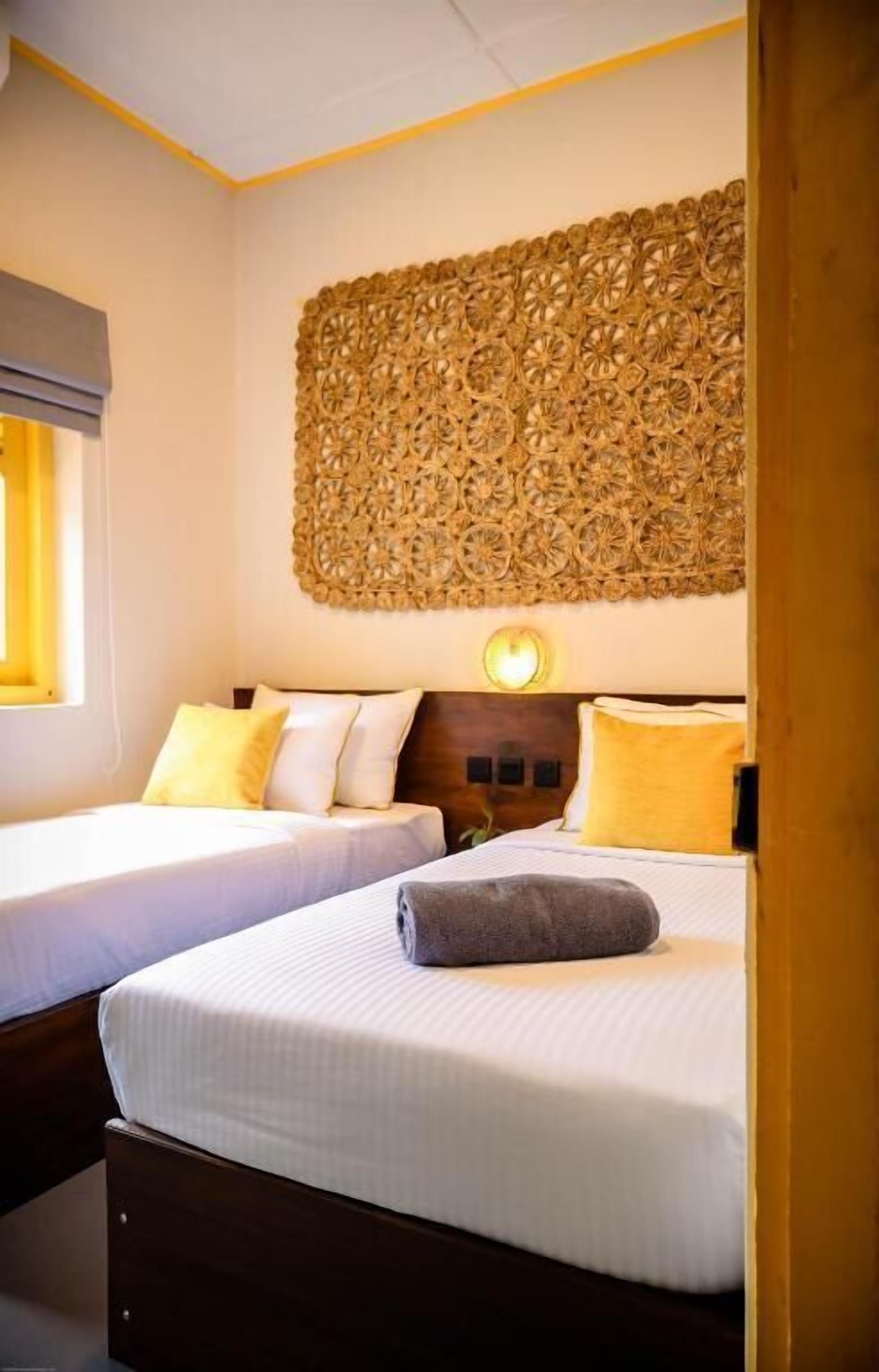 A hotel room with two beds, a decorative wall panel, and a bedside lamp.