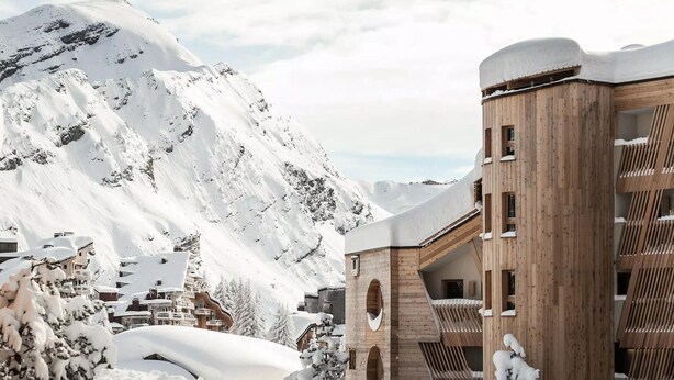 Un paisaje montañoso cubierto de nieve con una construcción de madera que cuenta con varios balcones y una base de piedra.