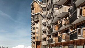 Un hotel de varios pisos con un diseño arquitectónico único, con balcones de madera y una montaña nevada al fondo.