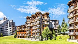 Un edificio de madera de varios pisos, con balcones, rodeado de césped y árboles.
