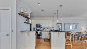 A spacious kitchen with white cabinetry, a central island, and a dining area with mismatched chairs. - Hightide Oasis is a bright, coastal getaway short walk to the beach. (Carolina Beach)