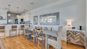 A modern kitchen with a dining area, wooden flooring, and a large mirror above the table. - Hightide Oasis is a bright, coastal getaway short walk to the beach. (Carolina Beach)