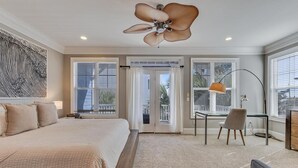 A bedroom with a large bed, a desk, and a chair. There is a ceiling fan, a window with blinds, and a door leading to a balcony. - Hightide Oasis is a bright, coastal getaway short walk to the beach. (Carolina Beach)