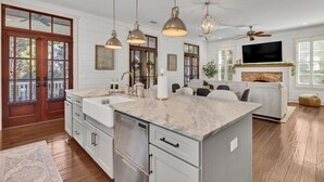 A spacious kitchen with a large island, pendant lights, and a built-in TV. - Two Homes · Walk to Old Town · Fire Pit · EV (Bluffton)
