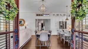 A modern kitchen with white cabinets, a wooden dining table, and a staircase leading to an upper level. - Two Homes · Walk to Old Town · Fire Pit · EV (Bluffton)