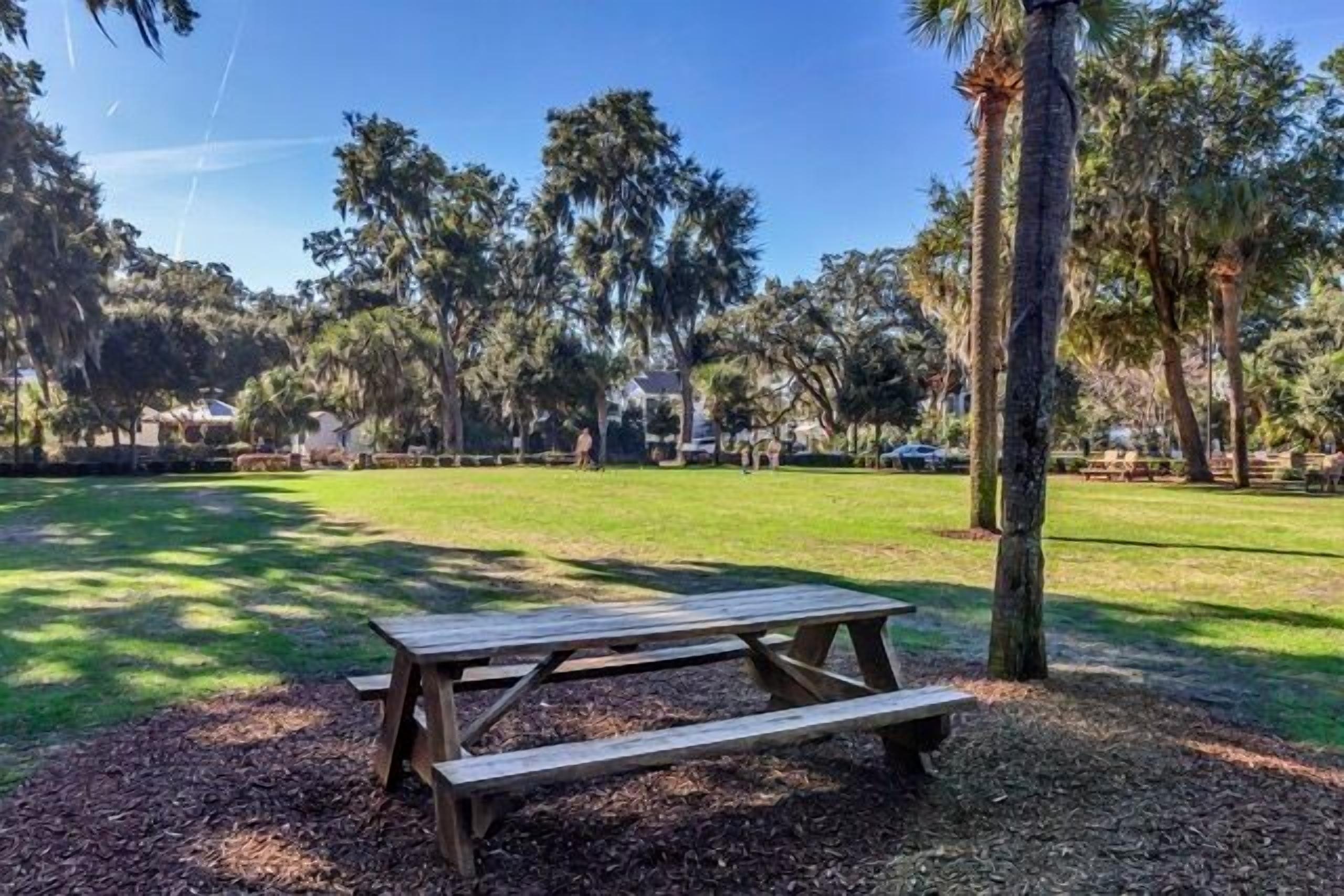 A picnic table in a park with trees and a clear sky.