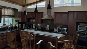 A kitchen with wooden cabinets, a large island with bar stools, pendant lights, and a stone backsplash.