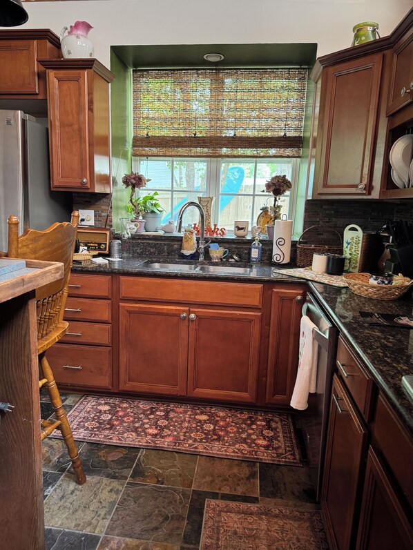 A kitchen with wooden cabinets, a granite countertop, a window with a view, and a rug on the floor. - Rustic Lakefront Retreat (Leesville)