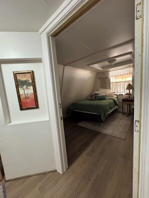 A bedroom with a bed, a nightstand, a lamp, and a painting on the wall. - Rustic Lakefront Retreat (Leesville)