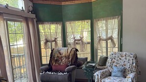 A cozy room with wooden ceiling, green walls, two windows with curtains, a sofa, a chair, and a small table.
