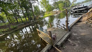 A wooden dock extending over a calm body of water, surrounded by trees and a grassy area.