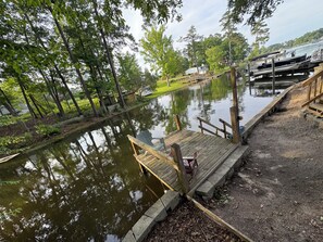 A wooden dock extending over a calm body of water, surrounded by trees and a grassy area.