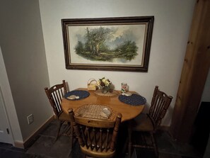 A dining table with a painting above it, surrounded by wooden chairs.