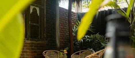 A covered outdoor seating area with wicker furniture and a brick wall.