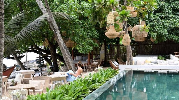 A poolside area with lounge chairs, a dining table, and hanging wicker baskets. - Banana Bunks Mirissa (Mirissa)