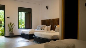A modern bedroom with two beds, a potted plant, and a view of greenery outside. - Banana Bunks Mirissa (Mirissa)