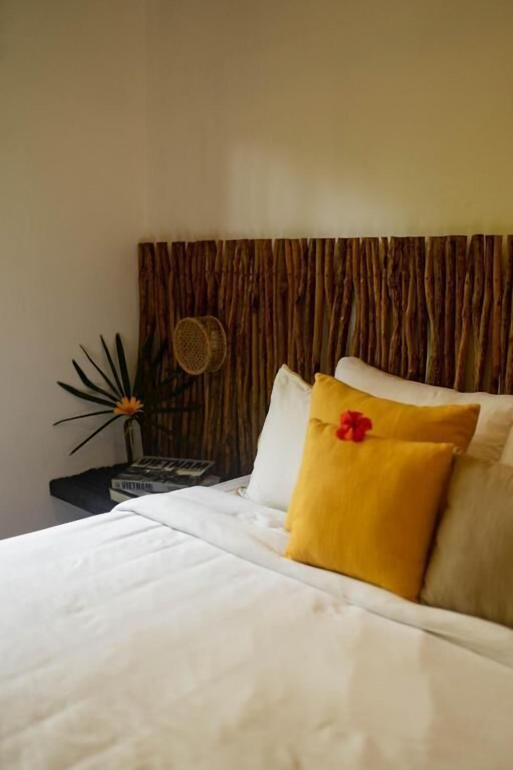 A neatly made bed with white bedding and a single yellow pillow with a red flower.