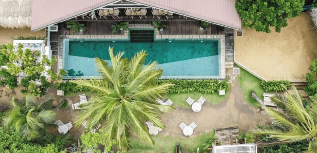 An aerial view of a resort with a swimming pool, lounge chairs, and palm trees.