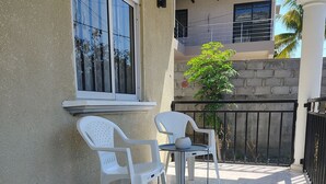 En balkon med to hvide plastikstole og et lille bord, et vindue samt udsigt til en nabobygning.